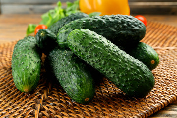Composition of cucumbers, tomatoes and sweet peppers on wicker serviette against wooden background