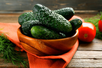 Fresh cucumbers with red cotton serviette and tomatoes on wooden table