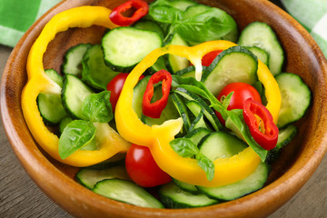 Vegetable salad with cucumbers  on wooden background decorated with green checked cotton serviette and sweet pepper