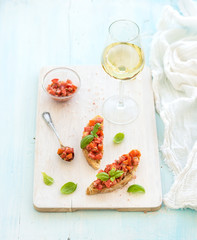 Tomato and basil bruschetta sandwich on white wooden serving board over rustic blue background, top view