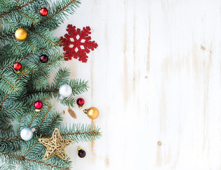 Christmas or New Year decoration background: fur-tree branches, colorful glass balls and glittering stars on white wooden background, top view