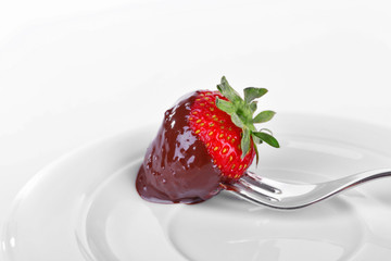 A fork and a strawberry in chocolate isolated on white