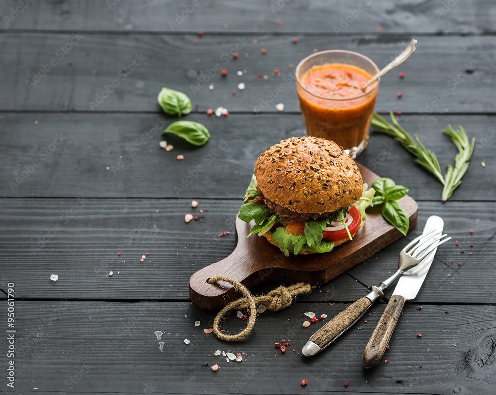 Wall mural fresh homemade burger on dark serving board with spicy tomato sauce, sea salt and herbs over black w