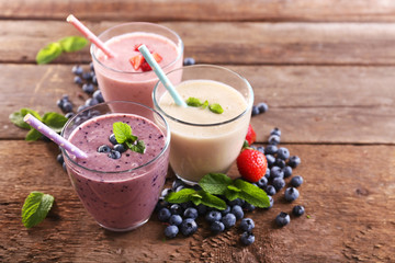 Tasty blueberry, strawberry and milk yogurts with berries and mint around on wooden background