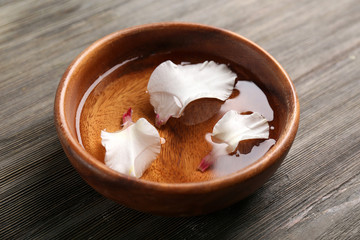 Flower petals in bowl with water on wooden background