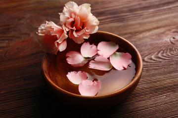 Pink rose petals in a bowl of water on wooden background