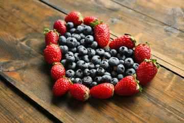 Heart shaped strawberries and blueberries on wooden background