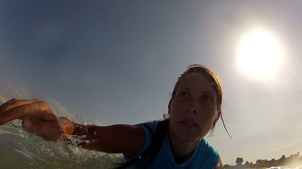 CLOSE UP: Young female surfer jumps on surf and starts paddling