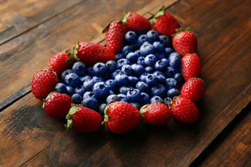 Heart shaped strawberries and blueberries on wooden background