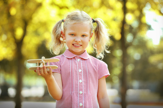 Blonde little girl plays with wooden plane at the park