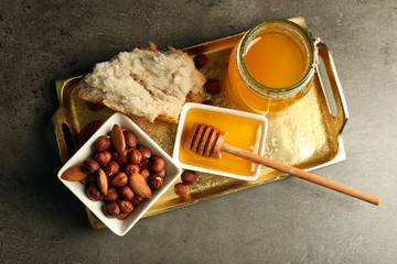 Glass jar and bowl with honey and nuts on gray background