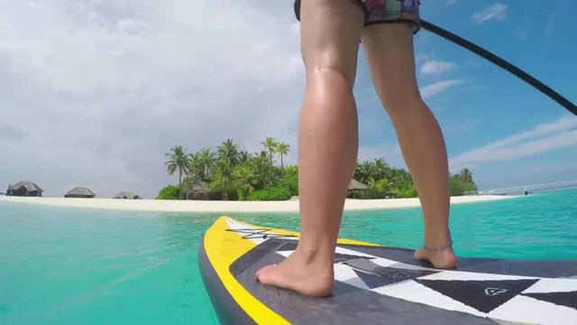 CLOSE UP: Female SUP boarding towards beautiful exotic Maldives island