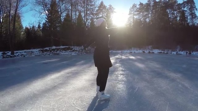 Young woman spinning on frozen lake on ice skates
