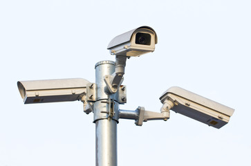 Three security cameras against the blue sky.