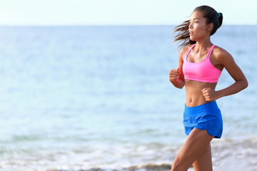 Fototapeta na wymiar Determined woman jogging on beach. Fit young female is in sports clothing. Jogger is exercising against ocean during sunny day.
