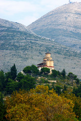 Fototapeta premium View of the Church of St. Michael the Archangel in Trebinje, Bosnia and Herzegovina: a small temple built on a hill with mountains in the background.