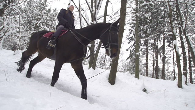 SLOW MOTION: Woman horseback riding in snowy forest