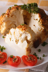 whole baked cauliflower and tomatoes close-up on a plate. vertical
