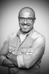 Hombre calvo de mediana edad con gafas rojas sonriendo. Blanco y negro.