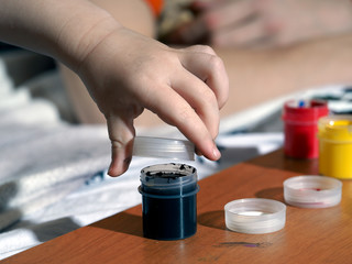 рука маленького ребенка и черная краска, гуашь. Малыш собирается рисовать черной краской