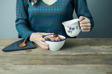young woman pouring milk into cereal for breakfast on wooden table