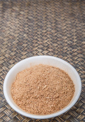 Dried galangal powder in a white bowl over wicker background