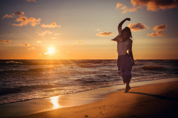 Happy woman barefoot on the beach at sunset.