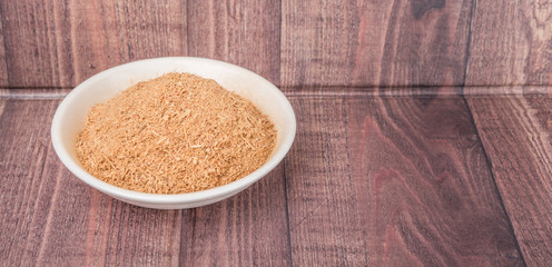 Dried galangal powder in white bowl over wooden background