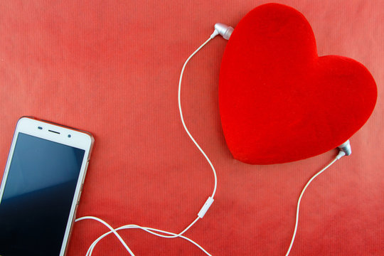 Heart with smartphone and earphones closeup on red