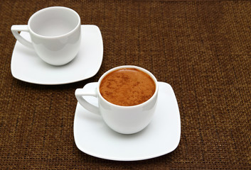 Two white cups with greek coffee on a sacking. Dark background