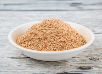 Dried galangal powder in white bowl over wooden background