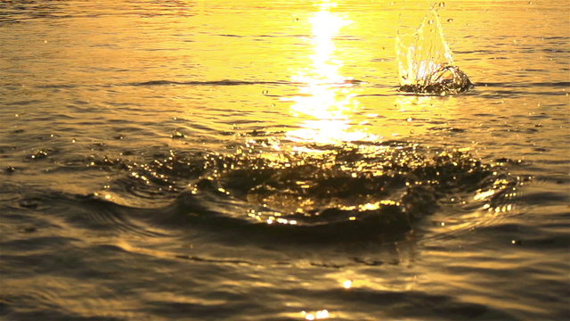 SLOW MOTION:Throwing a stone in the water at sunset