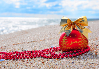 Red christmas bauble with golden bow on sand on beach