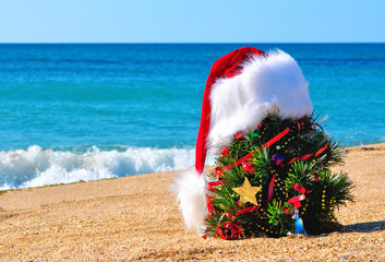 Christmas tree and santa hat on sand on beach