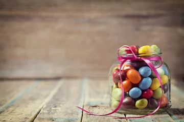 Fototapete Süßigkeiten Colorful candy jar decorated with a bow against rustic wooden background, birthday concept