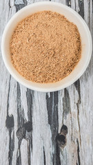 Dried galangal powder in white bowl over wooden background