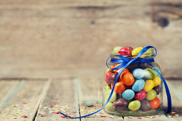 Colorful candy jar decorated with a bow against rustic wooden background, birthday concept - Powered by Adobe