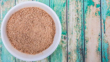 Dried galangal powder in white bowl over wooden background