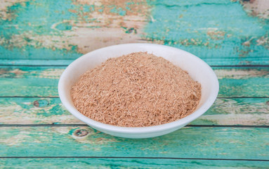 Dried galangal powder in white bowl over wooden background