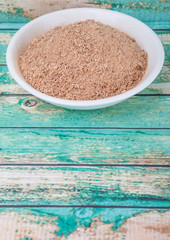 Dried galangal powder in white bowl over wooden background
