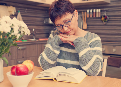 Woman 50 Years Old Reading A Book In The Kitchen