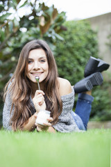 Healthy smiling woman laying on grass, eating yoghurt on spoon.