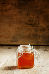 Amber dark honey in a glass jar on the old wooden table, selecti
