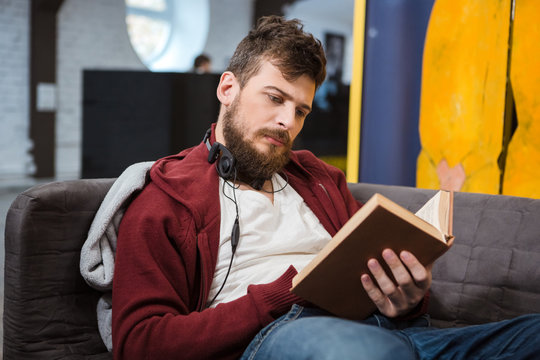 Serious guy sitting on sofa and reading a book