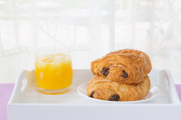 croissants with chocolate filling on a white plate, orange juice for pink. French pastries. side and top view, high key.