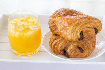 croissants with chocolate filling on a white plate, orange juice on a white tray. breakfast. French pastries. side and top view, high key.