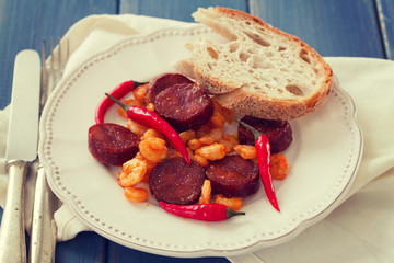 fried shrimps with sausages and red pepper on white plate on blue background