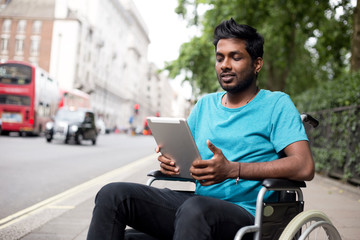 Disabled man in a wheelchair using a tablet computer in the street