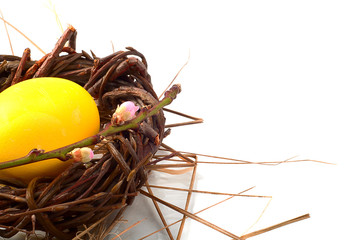 yellow Easter egg in a wicker wreath and with a branch of a blos