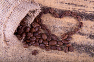 Heart from coffee beans close-up with a canvas sack on wooden te